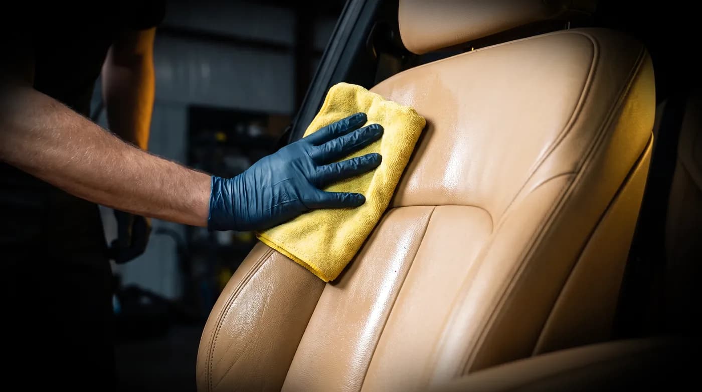 Wiping down a tan leather seat in a freshly cleaned cabin